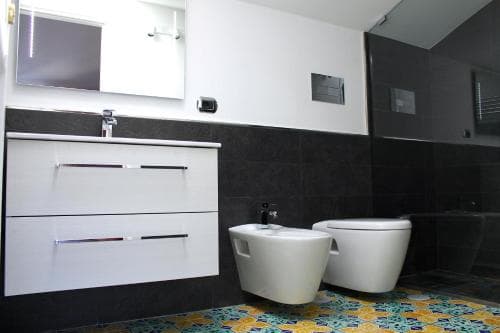 A modern bathroom with sleek white fixtures against dark tiled walls, vibrant patterned flooring, and a minimalist design evokes a serene and stylish atmosphere, ideal for travelers seeking contemporary accommodations.
