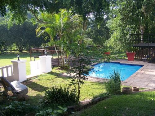 A serene tropical garden with a vibrant blue pool surrounded by lush greenery, palm trees, and cozy seating areas, ideal for a relaxing vacation retreat.