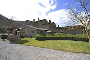 A serene countryside estate with stone buildings, lush greenery, and a gravel driveway invites travelers seeking a tranquil rural retreat.
