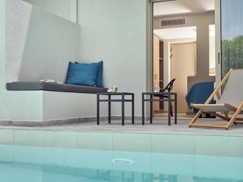 A serene hotel patio features a tranquil poolside area with lounge chairs, a cushioned bench, and modern furnishings, ideal for relaxing retreats.