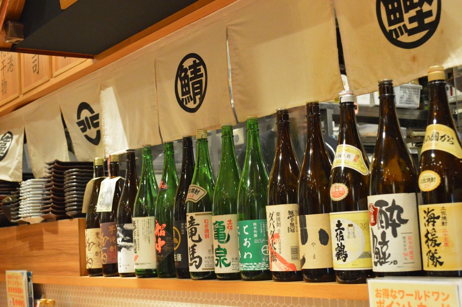A cozy Japanese izakaya in Tokyo's Ueno district displays an array of sake bottles under traditional banners, inviting travelers to explore its authentic culinary and drinking culture.