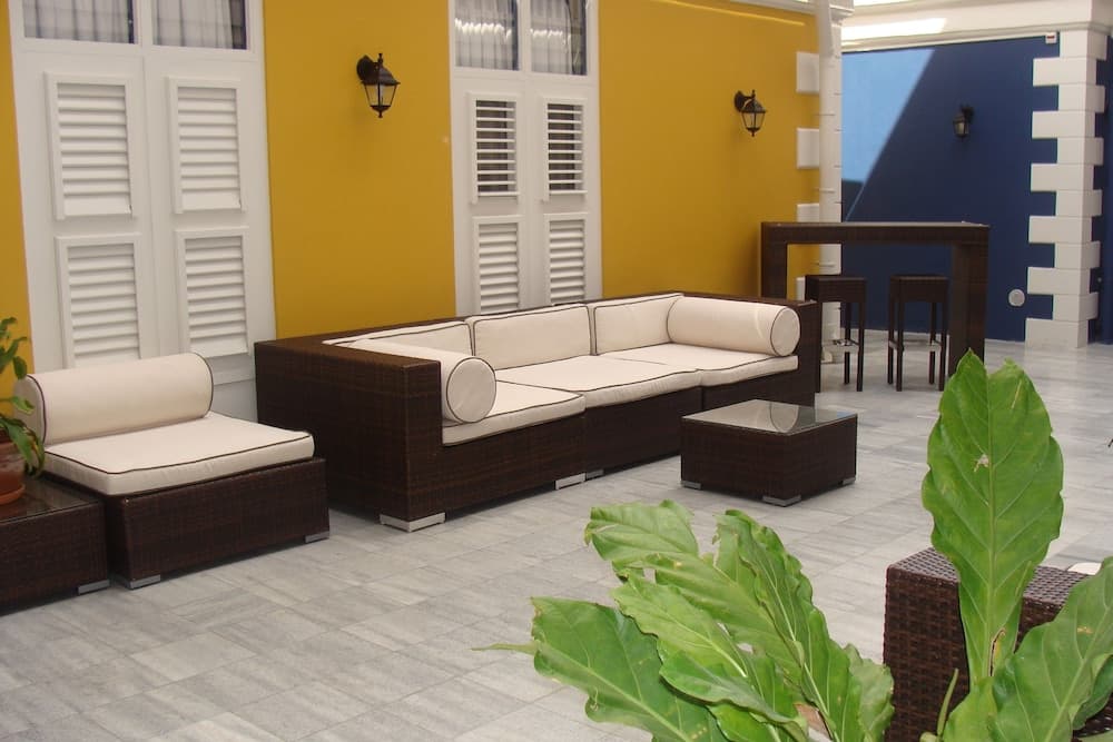 A cozy outdoor patio features comfortable wicker furniture against a vibrant yellow wall with white shutters, creating an inviting tropical retreat perfect for relaxation or social gatherings.