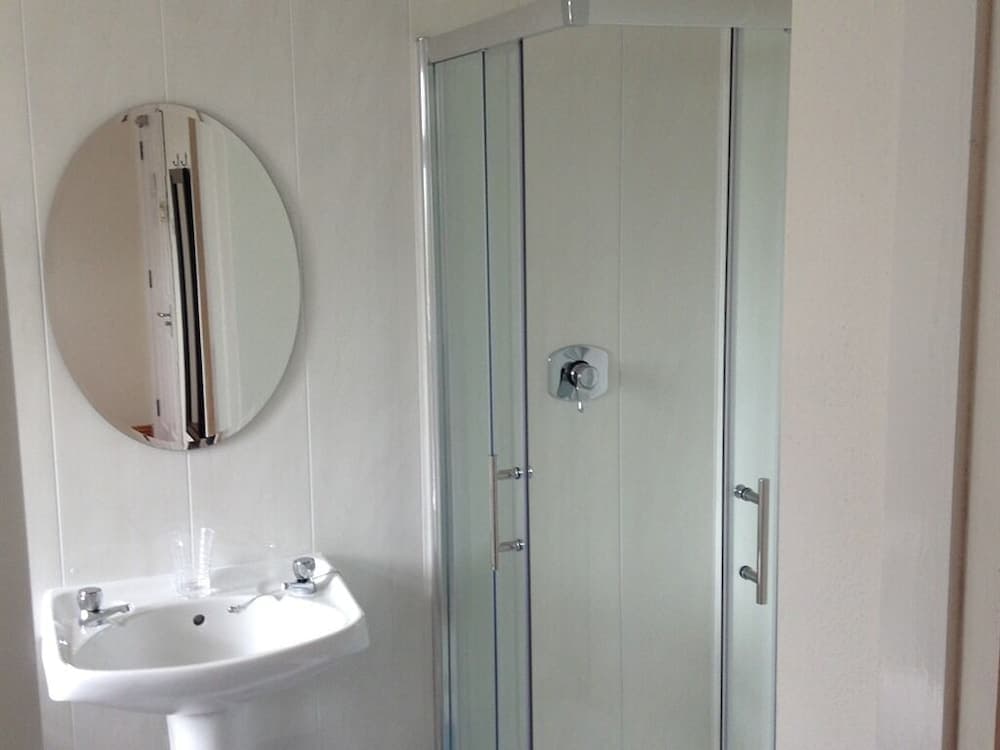 A compact bathroom features a sleek glass shower enclosure, a white pedestal sink, and a round mirror, ideal for travelers seeking efficient and modern amenities in a small space.