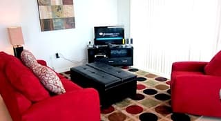 A cozy living room with vibrant red sofas, patterned cushions, and a stylish rug creates a warm and inviting atmosphere, perfect for travelers seeking comfort in a modern apartment setting.