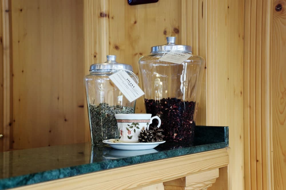 A cozy cabin interior features glass jars filled with dried herbs and flowers on a wooden shelf, accompanied by a floral teacup, evoking a serene and rustic atmosphere ideal for a relaxing getaway.