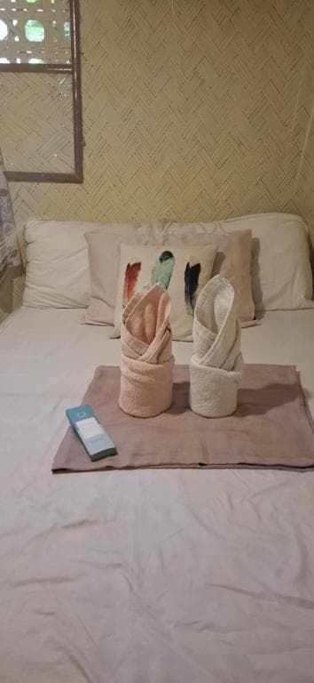 A cozy bedroom with bamboo walls and neatly folded towel bunnies on the bed evokes a serene and inviting atmosphere, perfect for travelers seeking relaxation in a rustic retreat.