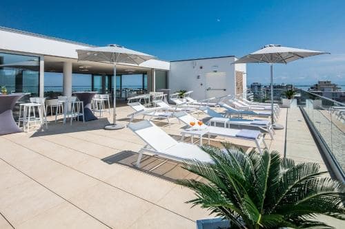 A serene rooftop terrace features lounge chairs, umbrellas, and a panoramic city view, ideal for travelers seeking relaxation and social gatherings in an urban setting.
