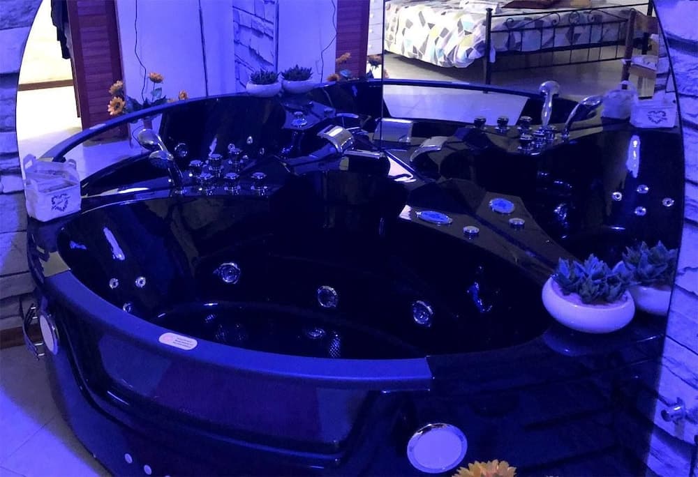A luxurious black hot tub with ambient blue lighting sits invitingly in a cozy indoor setting, surrounded by decorative plants and modern furnishings, perfect for a relaxing spa retreat.