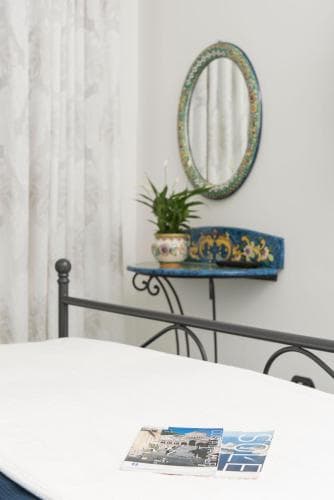 A cozy bedroom with a white bed, ornate mirror, decorative table, and potted plant exudes a serene and inviting atmosphere, perfect for travelers seeking a tranquil retreat.