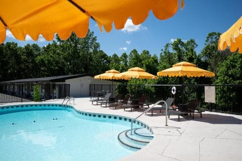 A serene outdoor pool area surrounded by lush greenery features vibrant yellow umbrellas and lounge chairs, ideal for relaxing vacations or family getaways.