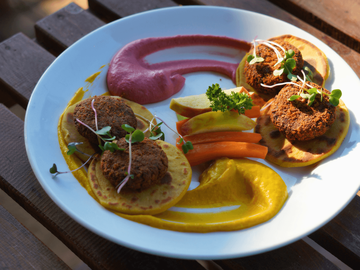 A vibrant plate of falafel, colorful sauces, and fresh vegetables on a wooden table captures the inviting and relaxed beachside dining experience at Chia · The Kitchen at Nalanda in Mandrem, Goa, perfect for travelers seeking a taste of local cuisine by the sea.