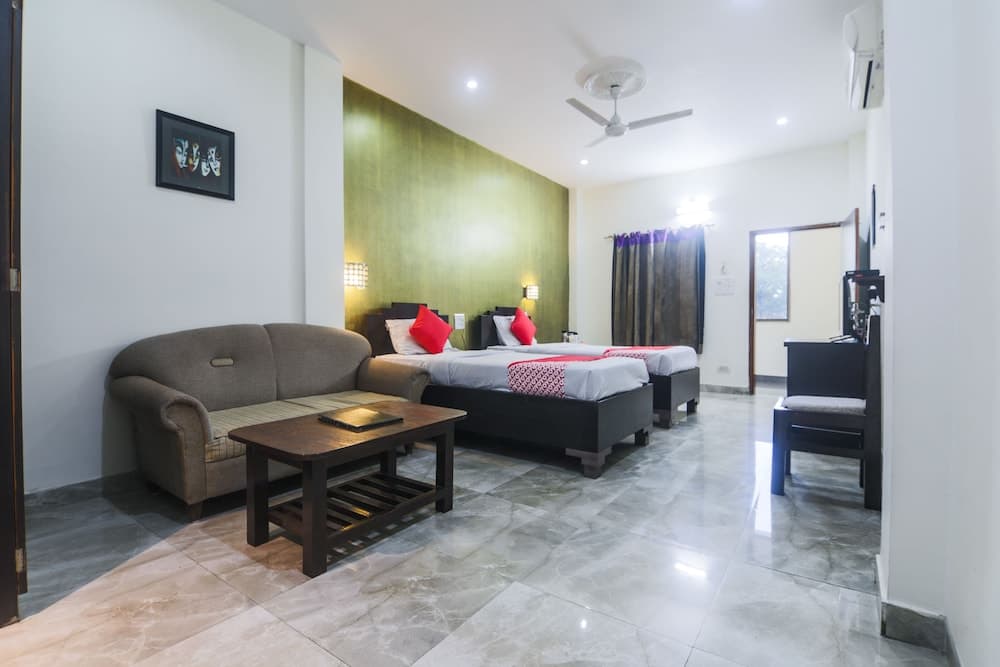 A cozy hotel room features two beds with red accents, a comfortable sofa, a wooden coffee table, and a green accent wall, creating a welcoming atmosphere ideal for travelers seeking relaxation.