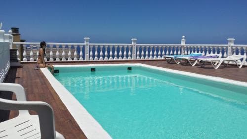 A serene rooftop pool area with turquoise water, white lounge chairs, and a scenic ocean view offers a relaxing retreat for vacationers seeking sun and leisure.
