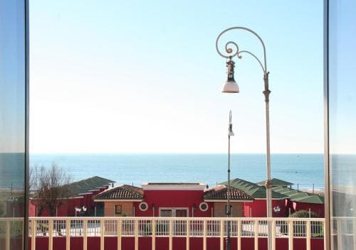 A serene coastal view framed by a balcony railing showcases vibrant red-roofed buildings under a clear blue sky, ideal for travelers seeking a relaxing seaside retreat.
