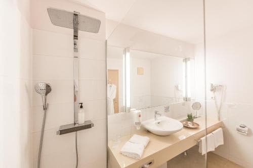 A modern hotel bathroom features a sleek glass shower enclosure, a large mirror, and a clean countertop with neatly folded towels, creating a bright and inviting atmosphere ideal for travelers seeking comfort and style.