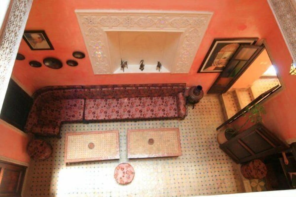 A cozy, ornately decorated room with vibrant pink walls, intricate ceiling designs, patterned cushions, and traditional rugs creates an inviting atmosphere ideal for cultural immersion and relaxation during travel.