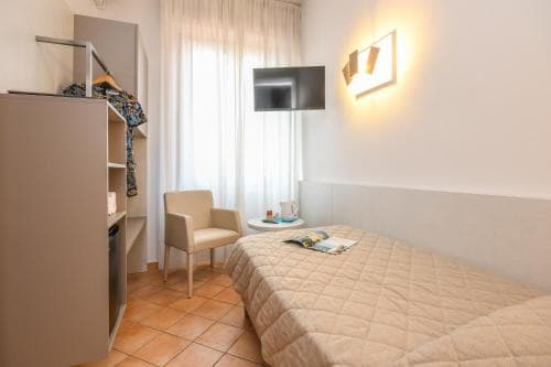 A cozy hotel room with warm lighting, tiled floors, a neatly made bed, and a small seating area creates an inviting atmosphere ideal for travelers seeking comfort and relaxation.
