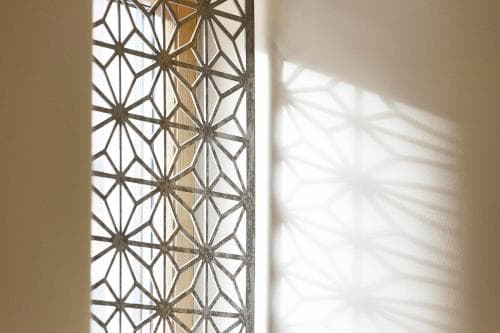 A serene indoor scene features intricate geometric patterns on a window casting delicate shadows on the wall, ideal for travelers seeking architectural inspiration or photography subjects.