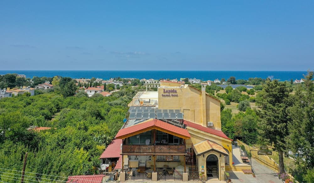 A serene coastal resort hotel with solar panels on its roof overlooks lush greenery and the vast blue sea, ideal for eco-conscious travelers seeking relaxation and scenic views.