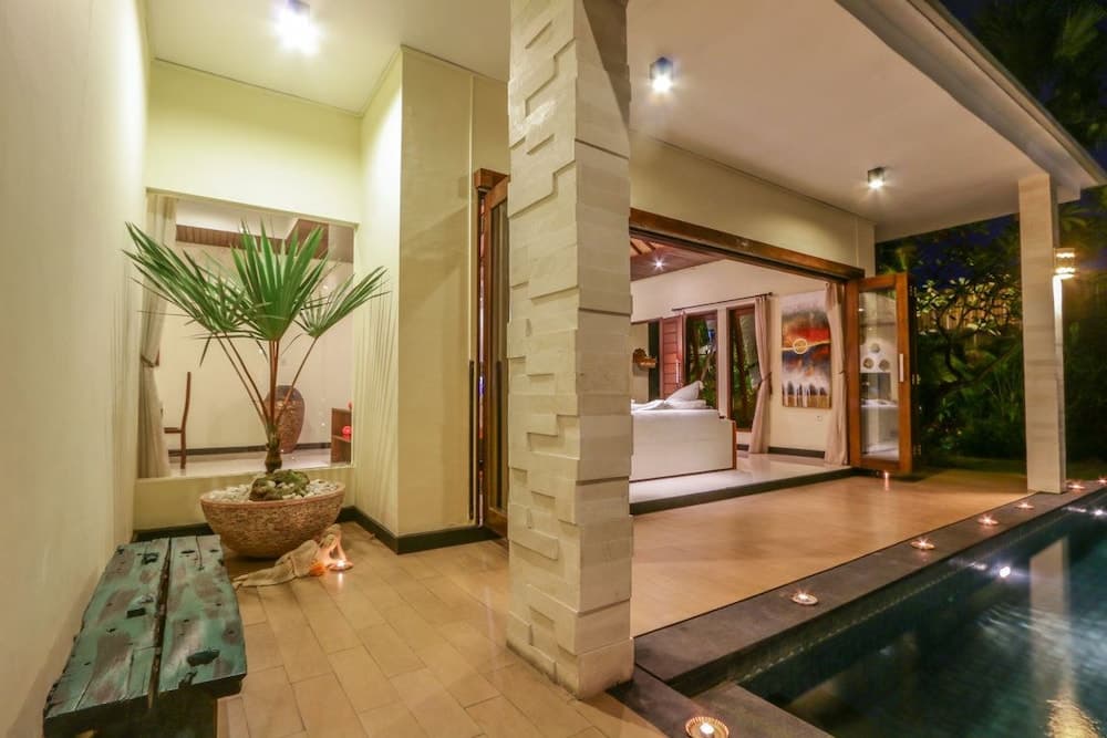 A serene tropical villa entrance features a tranquil indoor-outdoor space with a pool, floating candles, lush greenery, and warm lighting, ideal for luxury retreats and romantic getaways.