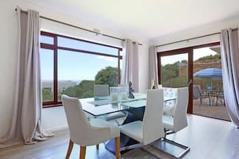 A bright, modern dining area with large windows overlooking lush greenery invites travelers to enjoy a serene meal in a cozy vacation rental setting.