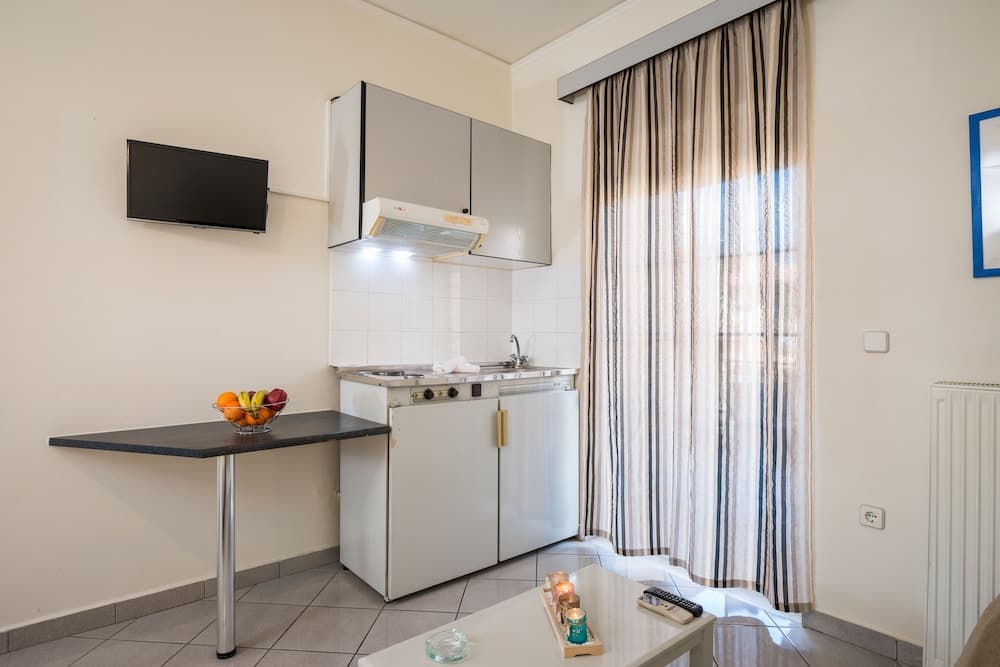 A cozy apartment kitchenette features a compact white stove, sleek cabinets, a small dining table with fruit, and striped curtains, ideal for travelers seeking a self-catering stay in an urban setting.