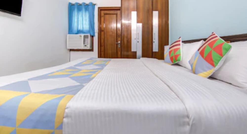 A cozy hotel room features a neatly made bed with colorful geometric bedding, wooden furniture, and a blue curtain, ideal for travelers seeking comfort and simplicity.