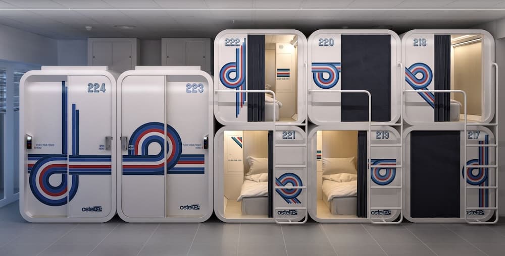 A modern capsule hotel room features sleek white pods with vibrant blue and red designs, offering travelers a cozy and efficient sleeping space in a compact urban setting.
