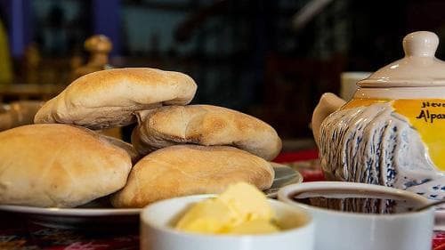 A cozy café scene featuring freshly baked bread rolls, butter, and a traditional teapot, evoking warmth and comfort ideal for a leisurely breakfast outing.