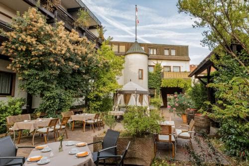 A serene outdoor dining area surrounded by lush greenery and a charming gazebo creates an inviting atmosphere for travelers seeking relaxation and leisure in a picturesque courtyard setting.