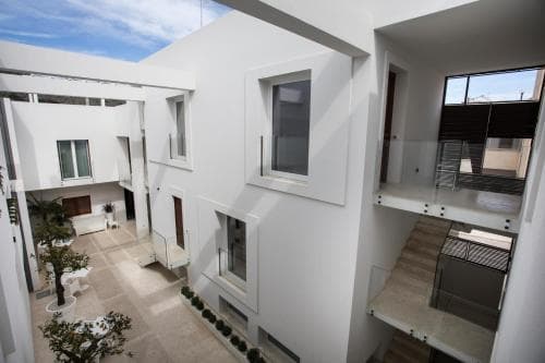 A serene courtyard of a modern white building features glass railings, potted plants, and a staircase, ideal for travelers seeking a tranquil urban retreat.