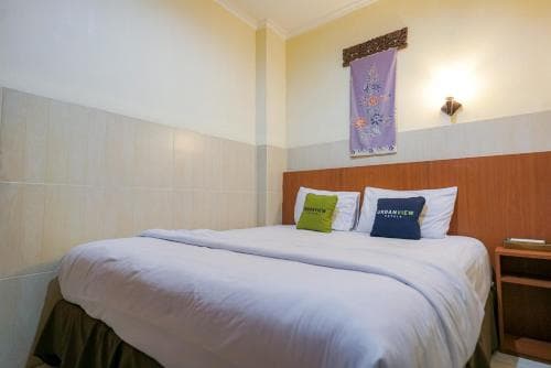 A cozy hotel room features a neatly made bed adorned with colorful pillows, a decorative tapestry on the wall, and warm lighting, ideal for travelers seeking comfort and relaxation.