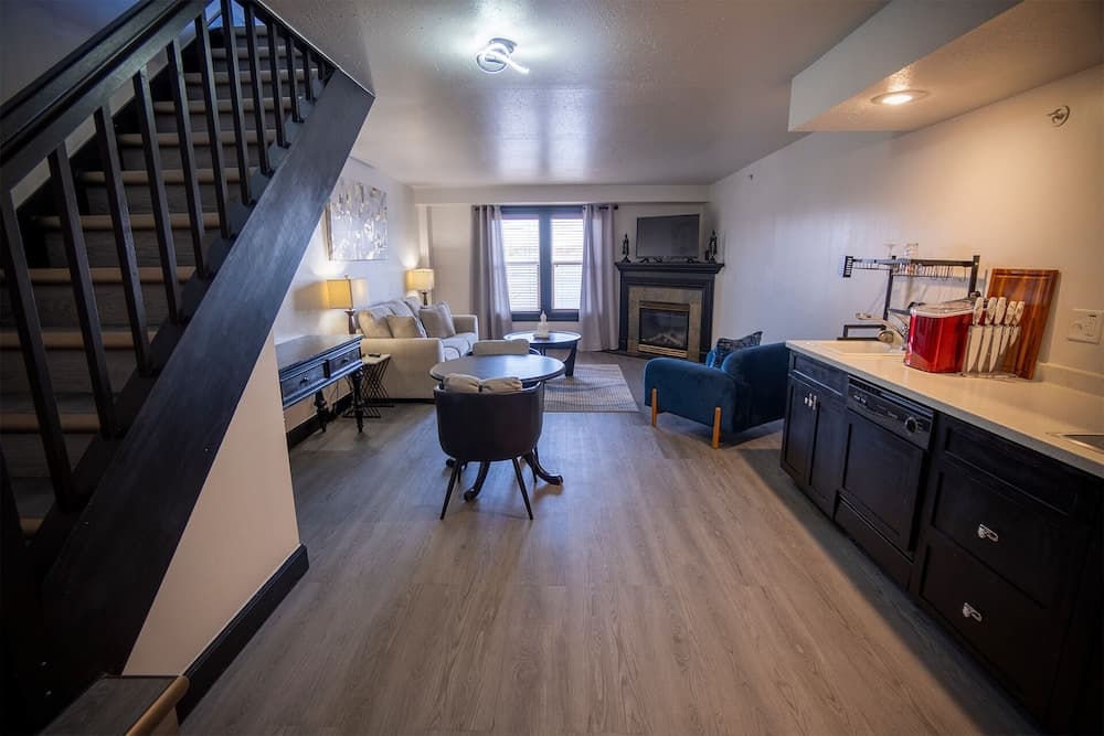 A cozy apartment interior featuring a staircase, modern kitchenette, living area with a fireplace, and ample natural light, ideal for travelers seeking comfort and convenience in a compact space.