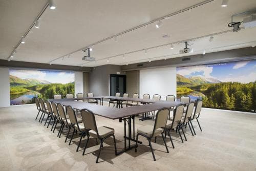 A spacious conference room with panoramic mountain murals exudes a serene atmosphere, featuring long tables, chairs, and modern lighting, ideal for professional retreats or team-building workshops.