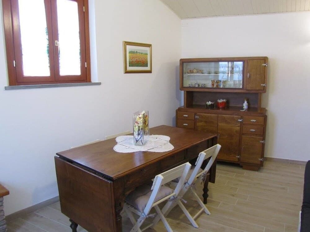 A cozy dining room with a wooden table set for two, a glass-fronted cabinet displaying decorative items, and a bright window, ideal for a serene vacation retreat.