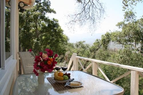 A serene balcony overlooking lush greenery offers a tranquil retreat with a table set for breakfast, ideal for a relaxing getaway in nature.