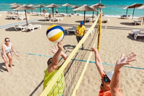 A lively beach volleyball game unfolds under sunny skies, with players in vibrant attire competing near a net on sandy shores lined with umbrellas and lounge chairs, perfect for a fun-filled vacation activity.