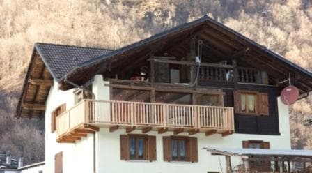 A cozy alpine chalet with wooden balconies and shutters nestles against a rugged mountain backdrop, evoking a serene winter retreat ideal for travelers seeking a peaceful escape.