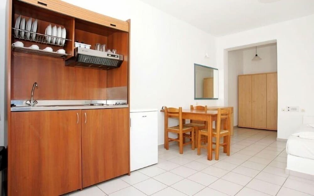 A cozy studio apartment features a compact kitchenette with wooden cabinets, a dining table set for four, and a minimalist design, ideal for travelers seeking self-catering accommodations in an urban setting.