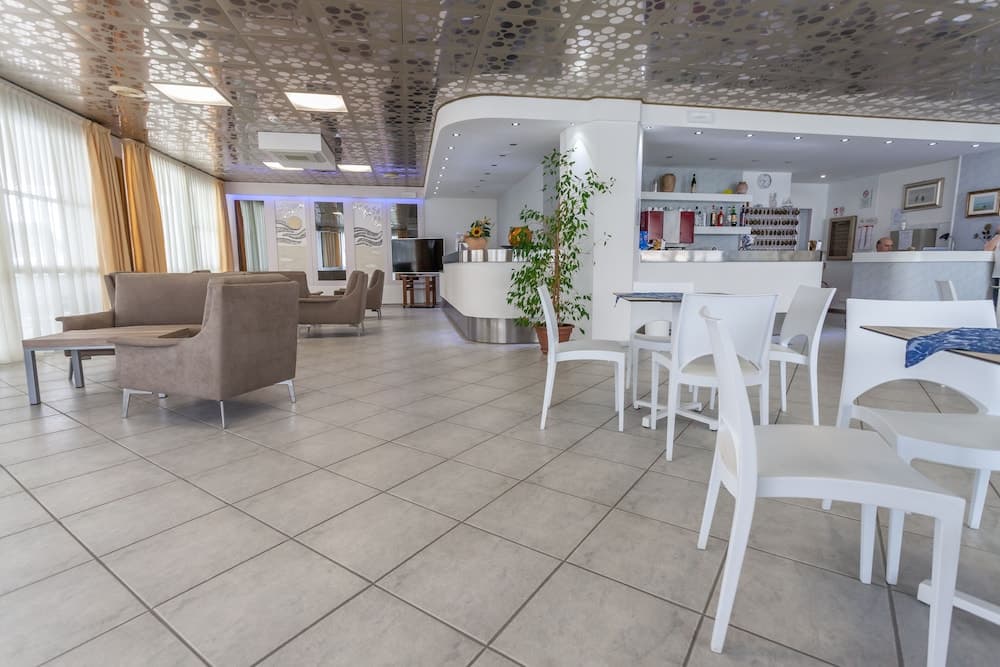 A modern, spacious hotel lobby features sleek white furniture, a stylish bar area, and large windows with curtains, creating an inviting atmosphere ideal for travelers seeking comfort and relaxation.