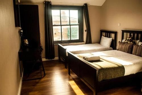 A cozy hotel room with two neatly made beds, wooden floors, and a window letting in natural light, ideal for travelers seeking comfort and simplicity.