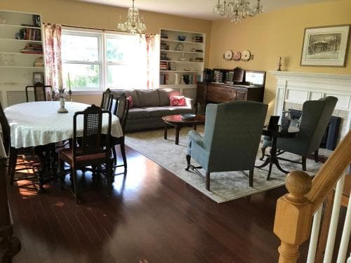 A cozy living room with hardwood floors, a round dining table, plush seating, and bookshelves bathed in natural light creates an inviting atmosphere ideal for family gatherings or a relaxing retreat.