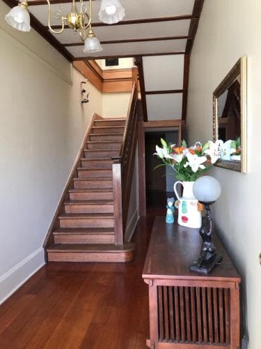 A cozy, warmly lit interior hallway features polished wooden stairs, vintage decor including a chandelier and floral arrangements, creating an inviting atmosphere ideal for exploring historic homes or boutique accommodations.