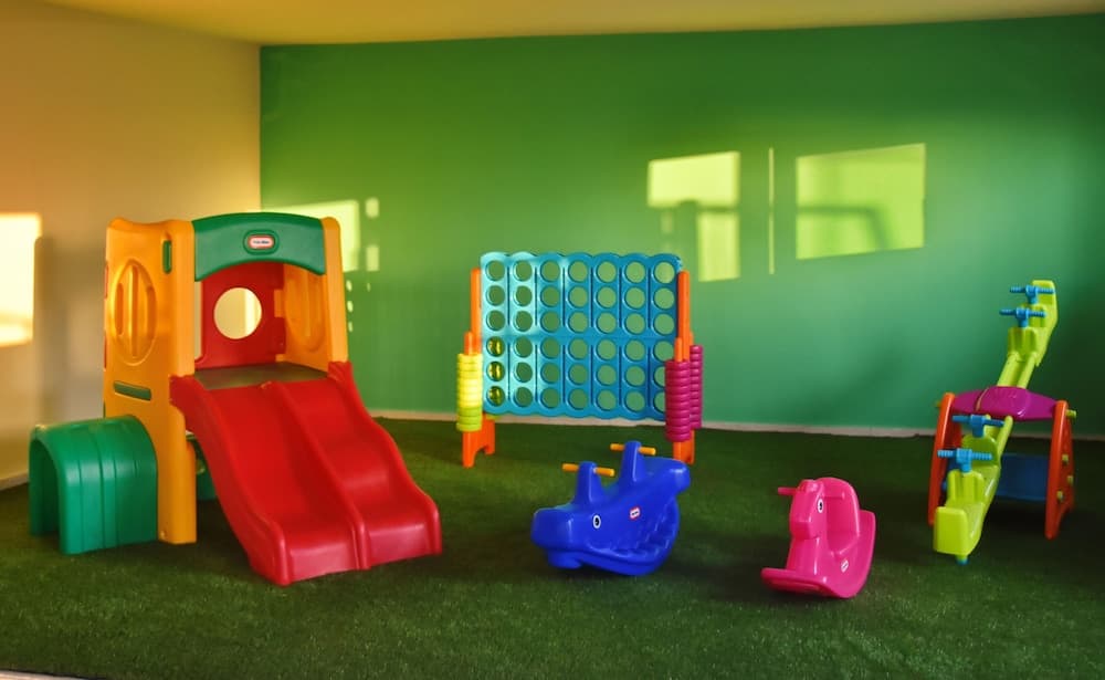 A vibrant indoor playroom features colorful toys like a slide, climbing frame, and ride-on animals on artificial turf, creating a cheerful atmosphere ideal for family-friendly accommodations.