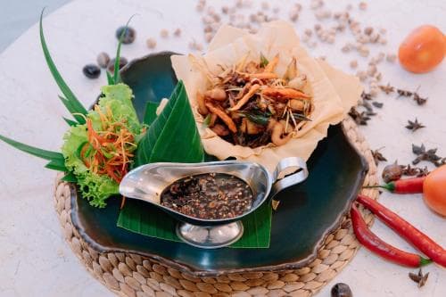 A vibrant tropical dish served on a woven mat with fresh herbs, chili peppers, and spices creates an inviting culinary experience ideal for food enthusiasts exploring exotic cuisines.