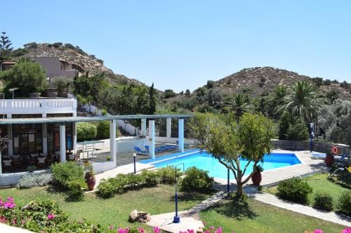 A serene resort pool area surrounded by lush greenery and hills under a clear blue sky, featuring lounge chairs and vibrant flowers, ideal for a relaxing vacation getaway.