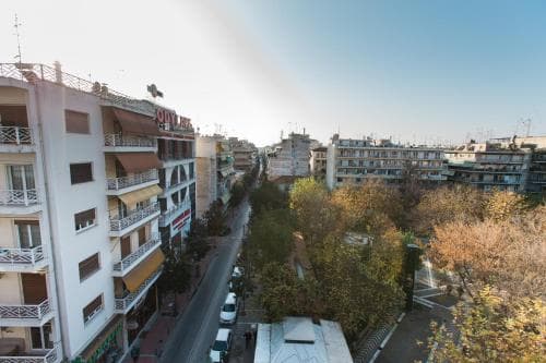 A serene urban street lined with balconied buildings and lush trees under a clear sky, ideal for city explorers seeking a blend of architecture and nature.