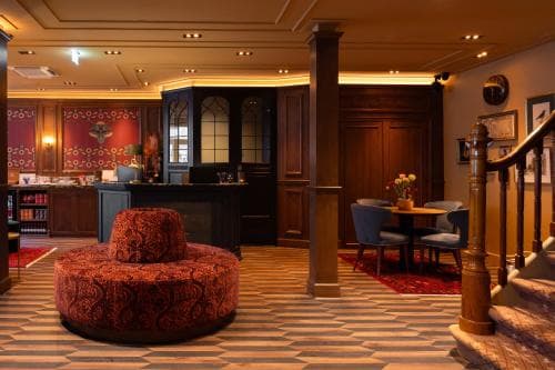 A cozy hotel lobby features ornate red seating, wooden paneling, and warm lighting, creating an inviting atmosphere ideal for travelers seeking relaxation and comfort during their stay.