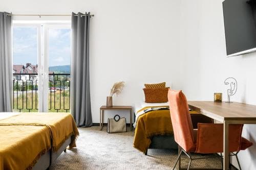 A cozy hotel room with vibrant orange accents, a balcony view of distant hills, and modern furnishings creates an inviting atmosphere ideal for travelers seeking comfort and relaxation.