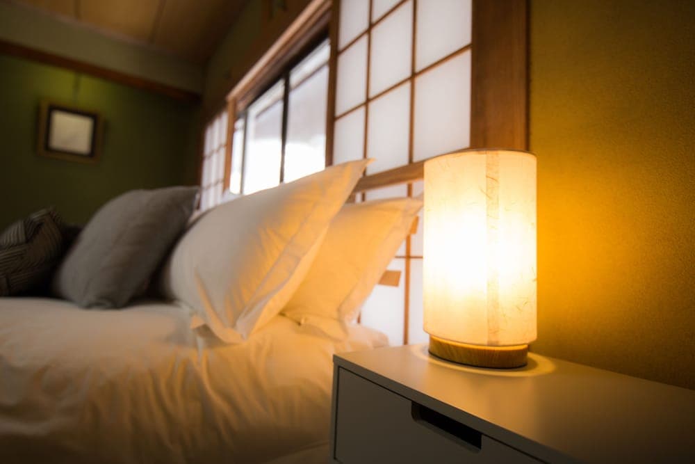 A cozy bedroom with soft lighting from a glowing bedside lamp creates a serene atmosphere, ideal for relaxation and sleep, featuring traditional sliding doors and plush bedding.
